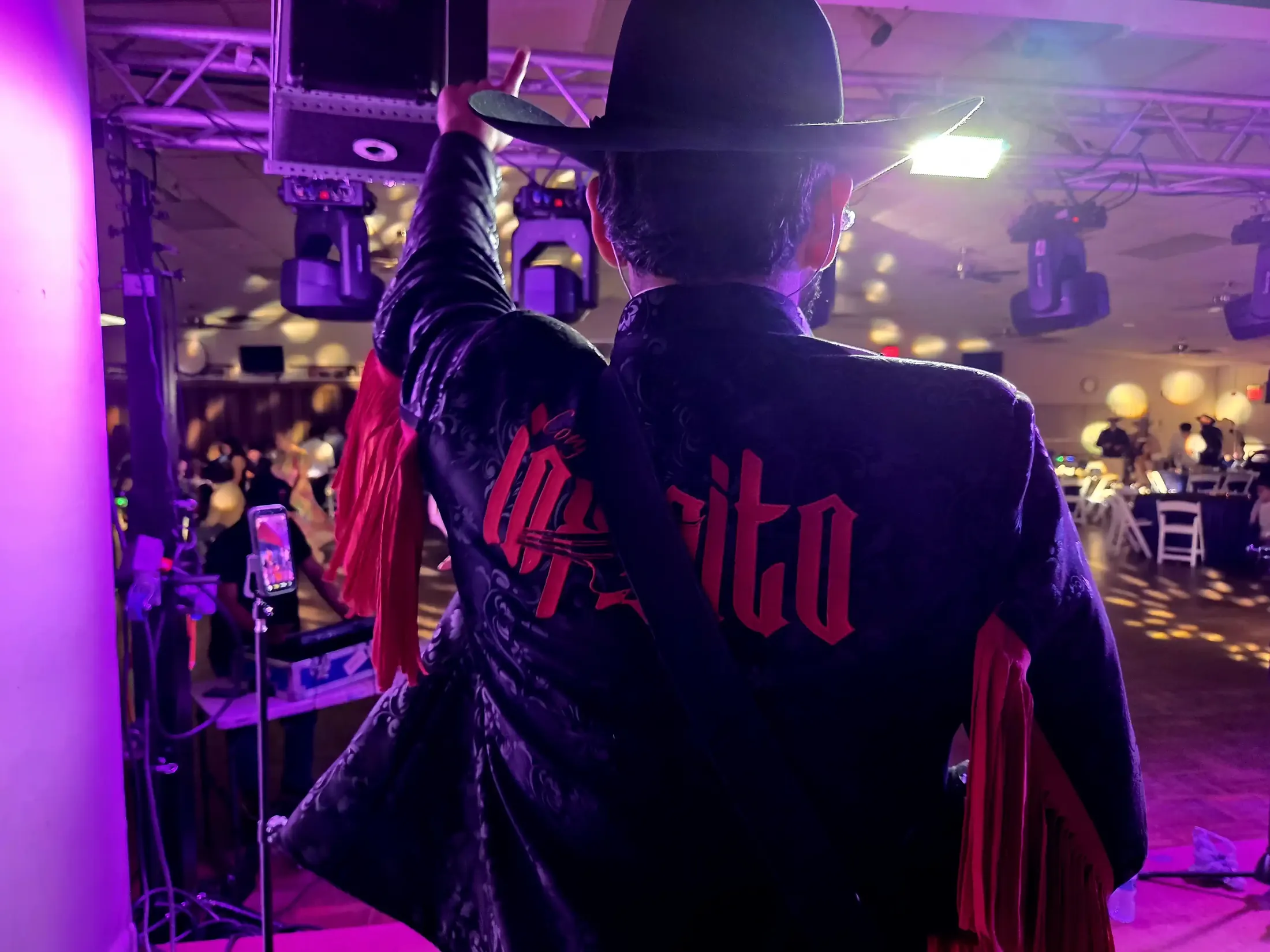 El cantante de Conjunto Infinito de espaldas, con su chaqueta bordada, frente al público del salón